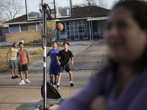 In this Jan. 24, 2018 photo, Claudia Mendez's son plays basketball with friends outside their home in Galena Park, Texas, as Mendez looks on, foreground. A gasoline spill about a mile away from Claudia Mendez's home forced the local fire department to put down foam in the neighborhood to suppress the fumes.