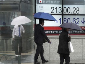 People walk past an electronic stock board showing Japan's Nikkei 225 index at a securities firm in Tokyo Tuesday, March 20, 2018. Asian shares slumped Tuesday as pessimism followed an overnight drop in New York amid a rout in technology companies.
