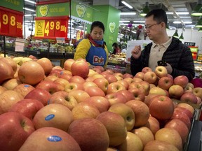 A woman wearing a uniform with the logo of an American produce company helps a customer shop for apples a supermarket in Beijing, Friday, March 23, 2018. China announced a $3 billion list of U.S. goods including pork, apples and steel pipe on Friday that it said may be hit with higher tariffs in a spiraling trade dispute with President Donald Trump that companies and investors worry could depress global commerce.