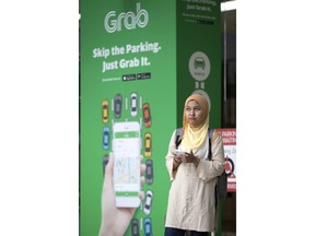 Passengers wait for Grab car outside a shopping man in Kuala Lumpur, Malaysia, Monday, March 26, 2018.  Ride-hailing giant Uber is selling its business in Southeast Asia to regional rival Grab in its latest withdrawal from a daunting overseas market. Grab, a fast growing Southeast Asian ridesharing, food delivery and financial services business, said Monday that Uber will take a 27.5 percent stake in it and Uber's CEO will have a seat on its board.