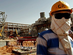 A worker covers his face to protect it from the dust and the blazing sun at the site of Saudi Aramco's oil processing facility in the Saudi Arabian desert.