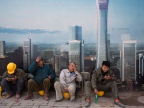 FILE - In this April 6, 2017, file photo, construction workers rest near a board with an artist's impression of the Central Business District outside a construction site in Beijing. The Asian Development Bank said in a report Wednesday, April 11, 2018, the bank is forecasting that developing Asian economies will expand slightly faster than expected this year but warns U.S. trade tensions are a major risk to its forecast.