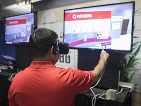 A Rogers employee wears VR goggles as he stands at a stall promoting VR retail over 5g, at a press event in Toronto on Monday, April 16, 2018, as Rogers Communications announced that it expects to test new high-speed 5G wireless networks in selected cities across Canada next year.