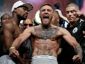 FILE - In this Aug. 25, 2017, file photo, Conor McGregor, center, stands next to Floyd Mayweather Jr., center left, during their weigh-in the day before their boxing match in Las Vegas. McGregor hit the headlines for the wrong reasons on Thursday, April 5, 2018, after being stripped of his UFC lightweight title. UFC president Dana White revealed at a press conference ahead of Saturday's card at the Barclays Center in New York that McGregor's 155-pound championship will be up for grabs, with the Irishman having not fought in the Octagon since winning his belt in November 2016. McGregor delivered a brief and to-the-point reaction on Twitter before later gatecrashing the UFC 223 media day, sparking chaotic scenes.