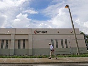 FILE- In this Oct. 12, 2017, file photo a pedestrian walks by a Comcast Service Center, in Miami. Comcast Corp. reports earnings Wednesday, April 25, 2018.