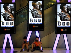 FILE - In this Aug. 10, 2017 file photo, children use smartphones near monitors displaying a Chinese action movie "Wolf Warrior 2" at a cinema in Beijing. Propelled by growth in China, global moviegoing reached a record high of $40.6 billion in 2017 despite a downturn in audiences at U.S. and Canada theaters.