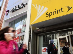 FILE- In this April 27, 2010 file photo, a woman using a cell phone walks past T-Mobile and Sprint stores in New York. T-Mobile and Sprint are trying again to combine in a deal that would reshape the U.S. wireless landscape, the companies announced Sunday, April 29, 2018