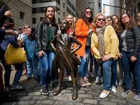 FILE - In this April 12, 2017 file photo, people gather at the "Fearless Girl" sculpture in lower Manhattan, New York. After she came to prominence staring down a symbol of Wall Street, a bronze bull at the foot of Broadway, New York City's Fearless Girl statue will be moving to a new home next to the New York Stock Exchange later in 2018.