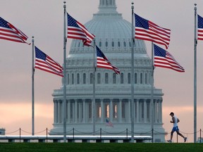FILE - In this Sept. 27, 2017, file photo, a early morning runner crosses in front of the U.S. Capitol as he passes the flags circling the Washington Monument in Washington. Congress returns from spring break Monday, April 9, 2018,  scrambling to compile a to-do list that will satisfy a president they desperately need to be touting their achievements, not undermining them, as they prepare to hit the campaign trail.
