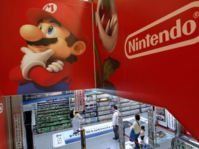 FILE - In this May 7, 2014, file photo, shoppers walk under the logo of Nintendo and Super Mario characters at an electronics store in Tokyo. Nintendo Co. is reporting solid sales and profit for the fiscal fourth quarter, powered by brisk demand for its Switch machines. The Japanese maker of Super Mario and Pokemon games reported Thursday, April 26, 2018,  that its January-March profit totaled 4.4 billion yen ($40 million), reversing a 394 million yen loss it racked up the previous year.