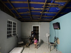 FILE - In this Dec. 21, 2017, file photo, two year old Yeinelis Oliveras González accompanies her father, Luis Oliveras, while eating dinner, in Morovis, Puerto Rico. The light blue glow cast by a tarp that covers half their roof, a donation from a church, has already dissipated. The Federal Emergency Management Agency awarded contracts to deliver hurricane supplies without adequately researching whether winning bidders could deliver what they promised, according to a new investigation by Democrats on a Senate oversight committee.