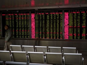 In this April 3, 2018 photo, a man walks electronic boards displaying stock trading index at a brokerage house in Beijing. Asian stock markets rose Monday, April 9, 2018,  amid uncertainty about an escalating U.S.-Chinese tariff dispute after President Donald Trump said a settlement was possible but his advisers said other nations might add to pressure on Beijing.