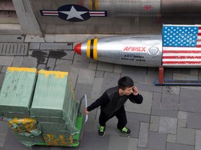 FILE - In this March 23, 2018, file photo, a delivery man calls for directions while pulling a cart of goods past a U.S. apparel store in Beijing, China. President Donald Trump's threat to hike tariffs on technology imports from China strikes at the heart of Beijing's state-led blueprint for prosperity and restoring the nation's greatness.