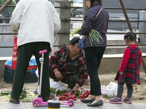 In this Monday, April 16, 2018 photo, a vendor sells vegetable along a street of Beijing, China's economic growth held steady at 6.8 percent over a year earlier in the quarter ending in March, buoyed by retail sales and investment, data released Tuesday, April 17, 2018.