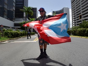 FILE - In this Aug. 30, 2017 file photo, a man holds a Puerto Rican flag to protest austerity measures as demonstrators march to the offices of a federal control board created by U.S. Congress last year, in San Juan, Puerto Rico. New austerity measures announced on Wednesday, April 18, 2018 call for a 10 percent average cut to pensions, seeks the closure of prisons, the consolidation of dozens of state agencies and significant reductions in government subsidies.