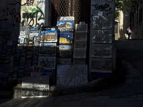A woman walks past pictures for sale depicting the Ancient Parthenon temple, in Plaka district of Athens, Tuesday, April 24, 2018. Lying under the shadow of the ancient Acropolis Hill, Plaka's narrow streets and neoclassical architecture have for decades attracted tourists and Athenians alike.