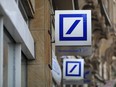The Deutsche Bank AG logo sits outside a bank branch in Frankfurt, Germany, on Wednesday, May 23, 2018. Deutsche Bank will cut a quarter of equities jobs and reduce overall positions by  at least 7,000 as Chief Executive Officer Christian Sewing seeks to slash costs and boost profitability at the investment bank.