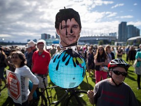 A protester holds a photo of Prime Minister Justin Trudeau and a representation of the globe covered in oil during a protest against the Kinder Morgan Trans Mountain Pipeline expansion in Vancouver, B.C., on Tuesday May 29, 2018.