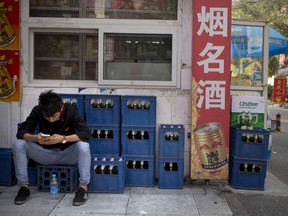 FILE - In this Thursday, Oct. 15, 2015, photo, a restaurant worker sits on crates of beer outside a convenience store as he uses his smartphone in Beijing. Hundreds of craft beer enthusiasts, investors and brewers are attending an exhibition in Shanghai dedicated to expanding the palette of Chinese consumers and promoting sales of high-end brews.