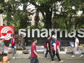 FILE - In this Oct. 1, 2017, file photo, people walks past Sinarmas Land Plaza during a car-free day at the main business district in Jakarta, Indonesia. Forest Stewardship Council, the main global group for certifying sustainable wood, has sent a come-clean ultimatum to Sinarmas, one of the world's largest paper companies following evidence it continues to cut down tropical forests and hide activities behind corporate proxies.