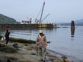 In this May 3, 2018 photo, a couple walk their dog on the shore near the Kinder Morgan Inc. Westridge oil tanker terminal in Burnaby, British Columbia, Canada. The company's Trans Mountain expansion is projected to increase oil tanker traffic here from about 60 vessels per year to more than 400, as the pipeline flow increases from 300,000 to 890,000 barrels per day.
