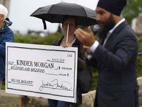 NDP Leader Jagmeet Singh speaks as a woman holds a novelty cheque made out to Kinder Morgan at a rally against the proposed Trans Mountain pipeline project, on Parliament Hill in Ottawa on Tuesday, May 22, 2018.
