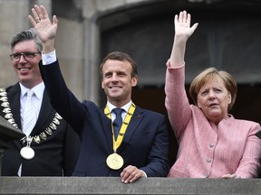 German Chancellor Angela Merkel and French President Emmanuel Macron wave from the town hall balcony on occasion of the Charlemagne Prize awarding in Aachen, Germany, Thursday, May 10, 2018. Left Aachen's mayor Andreas Herman.