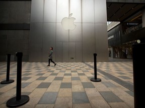 FILE- In this Oct. 20, 2017, file photo, a woman walks past the logo for an Apple Store at an outdoor shopping mall in Beijing, China. Apple Inc. reports earnings Tuesday, May 1, 2018.