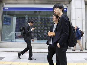 In this April 16, 2018, file photo, people walk by an electronic stock board of a securities firm in Tokyo. Tokyo stocks were marginally higher Tuesday, May 1, 2018,  while most other major Asian markets were closed for public holidays. The White House's announcement that it would postpone a decision on imposing hefty tariffs on U.S. imports of steel and aluminum products from some countries helped boost investor sentiment.