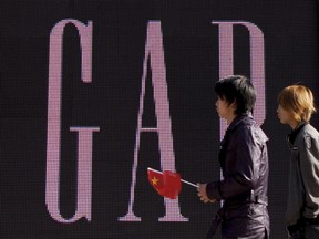 FILE - In this Nov. 16, 2010 file photo, a man carries a Chinese flag as he walks past U.S. retailer GAP's newly-opened flagship store in Beijing. U.S. clothing retailer Gap has apologized Monday, May 14, 2018, for selling T-shirts with what it says was an "erroneous" map of China.