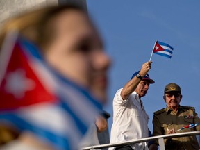 FILE - In this May 1, 2018 file photo, Cuba's President Miguel Diaz-Canel waves a Cuban flag next to former President Raul Castro as they watch the annual May Day parade file through Revolution Square in Havana, Cuba. Castro, who turned over the presidency to Diaz-Canel, has proposed a constitutional reform limiting presidents to two five-year terms and imposing an age limit, a dramatic shift following a nearly 60-year run of leadership by Castro and his late brother Fidel, who both ruled into their 80s.