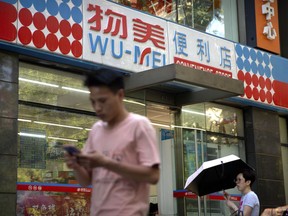 People walk past a Wumei convenience store, part of the Wumart Stores retail company, in Beijing, Thursday, May 31, 2018. China's supreme court has thrown out the fraud conviction of a retail tycoon in an unusual gesture of official leniency toward entrepreneurs amid a string of high-profile detentions and prosecutions that has rattled the Chinese business world.