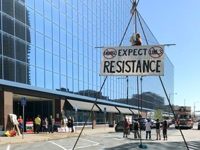 A protester from the Line 3 Resistance Project hangs from a metal tripod set up to block traffic on a street outside a downtown St. Paul, Minn., building on Thursday, June 28, 2018, where Minnesota regulators were to meet to consider whether to approve Enbridge Energy's proposal for replacing its aging Line 3 crude oil pipeline across northern Minnesota.