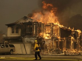 FILE - In this Oct. 9, 2017, file photo, a firefighter walks near a flaming house in Santa Rosa, Calif. A Northern California utility says it will take a $2.5 billion charge for expected losses in connection with deadly wildfires that whipped through the state's wine country in October. Pacific Gas & Electric on Thursday, June 21, 2018, also warned its liability could be considerably higher after state fire officials determine the cause of 21 major fires that rampaged throughout Northern California, killing 44 people and destroying thousands of homes and businesses.