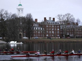 FILE-- In this March 7, 2017 file photograph, rowers pass the campus of Harvard University as they paddle down the Charles River in Cambridge, Mass.  Harvard and the group Students for Fair Admissions will file dueling analyses of the Ivy League school's admissions data in a lawsuit alleging discrimination against Asian-American applicants.