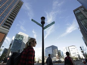 In this May 14, 2018 photo passers-by make their way along a street near an intersection in Boston's Seaport District. In this old city's booming Seaport District, General Electric is building its new world headquarters, Amazon is bringing in thousands of new workers, and Reebok's red delta symbol sits atop the new office it opened last year. Three businesses are testing self-driving cars, other dynamic companies are planting their flag, and trendy restaurants and apartments have gone up virtually overnight. But after bad flooding during a storm this past winter, critics wonder whether it was a bright idea to invest so much in a man-made peninsula that sits barely above sea level.