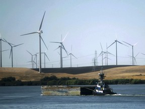 FILE - In this Sept. 23, 2013, file photo, a tugboat pushes a barge down the Sacramento River past wind turbines near Rio Vista, Calif. A contentious proposal to link oversight of California's electric grid with other western states faces a crucial test Tuesday, June 19, 2018, in a state Senate committee.