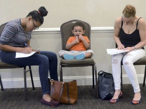 FILE- In this May 15, 2018, file photo, Joan Herrera, center, sits and waits as his mother Andrea Batista Garcia, left, and Marlene Gonzales, fill out job applications while attending the Great Northeast 2018 Job Fair at Capriotti's in McAdoo, near Hazleton, Pa. The U.S. government issues the May jobs report on Friday, June 1.