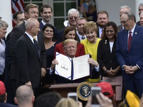 In this June 6, 2018, photo, President Donald Trump holds up the "VA Mission Act of 2018" that he signed during a ceremony in the Rose Garden of the White House in Washington.