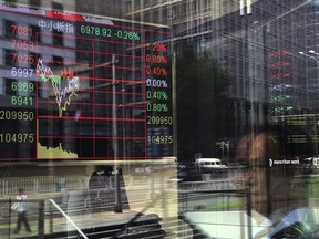 People and office buildings are reflected on a brokerage house's window as an electronic board displaying stock trading index in Beijing, Tuesday, June 12, 2018. Asian shares were mostly higher Tuesday but little changed as market players tried to digest the summit between President Donald Trump and North Korean leader Kim Jong Un in Singapore.