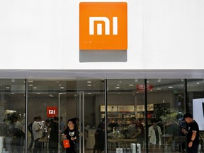 In this Wednesday, June 20, 2018, photo, a woman with purchased goods walks out from the Xiaomi store in Beijing. Xiaomi, a Chinese startup that helped to pioneer the trend toward ultra-low-priced smartphones, is preparing for what would be the biggest initial public offering since e-commerce giant Alibaba's in 2014. The 8-year-old is a star among the Chinese unicorns, a term that refers to startup companies that are valued at more than $1 billion. It has a dedicated Chinese fan base and its media-savvy leader is an Asian celebrity. But it is untested outside the region.