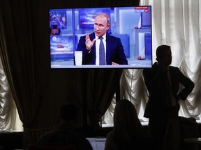 A journalist speaks on the phone while Russian President Vladimir Putin gestures answering a question during his annual call-in show in Moscow, Russia, Thursday, June 7, 2018. Putin says he's confident of Russia's long-term economic growth. Speaking at the opening of his annual call-in television show, Putin said on Thursday that Russia's gross domestic product is currently 1.5 percent higher than a year ago. He described it as modest but said he is confident that future "growth is guaranteed."