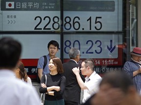 People walk by an electronic stock board of a securities firm in Tokyo, Thursday, June 14, 2018. Asian stock markets slumped on Thursday with South Koreans stocks plunging 1.6 percent on the first day of trading after an unprecedented summit between leaders of North Korea and the United States. Stocks plunged after Federal Reserved hiked its key rate and signaled an acceleration in its pace of rate increase.