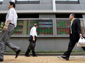 People walk past an electronic stock board of a securities firm in Tokyo, Thursday, June 14, 2018. Asian stock markets slumped on Thursday with South Koreans stocks plunging 1.6 percent on the first day of trading after an unprecedented summit between leaders of North Korea and the United States. Stocks plunged after Federal Reserved hiked its key rate and signaled an acceleration in its pace of rate increase.