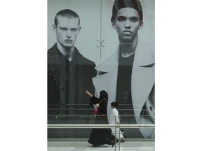 In this May 4, 2018 photo, a Qatari woman passes by a billboard advertising western clothing at a shopping mall in Doha, Qatar. A year into a blockade by four Arab states against Qatar, the small country has weathered the storm by drawing from its substantial financial coffers, using its strategic location in the Persian Gulf as the world's largest producer of liquefied natural gas to continue shipments to major world powers, and forging tight alliances with countries like Turkey and Iran.