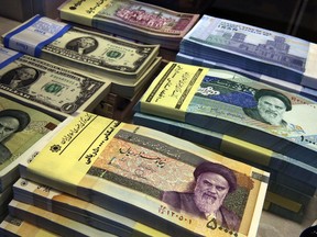 FILE - In this April 4, 2015 file photo, Iranian and U.S. banknotes are on display at a currency exchange shop in downtown Tehran, Iran. Iran's currency is continuing its downward spiral as increased American sanctions loom, hitting a new low on the thriving black market exchange. The Iranian rial fell to 112,000 to the dollar on Sunday, July 29, 2018, from 98,000 to $1 on Saturday.
