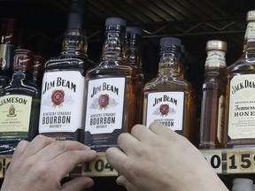 This July 9, 2018, photo shows a man adjusting prices under bottles of Jim Beam bourbon whiskey displayed at Rossi's Deli in San Francisco. China's government vowed Wednesday, July 11, to take "firm and forceful measures" as the U.S. threatened to expand tariffs to thousands of Chinese imports. After the U.S. imposed 25 percent tariffs on $34 billion worth of Chinese goods, China retaliated by imposing tariffs on the same amount of U.S. products including whiskey.