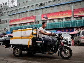 A man rides a motor-tricycle loaded with seafood products past by a billboard featuring Chinese President Xi Jinping and the government propaganda on display at the Jingshen seafood market in Beijing, Thursday, July 12, 2018.