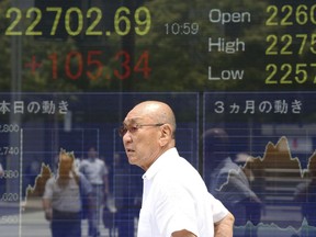 A man walks by an electronic stock board of a securities firm in Tokyo, Tuesday, July 17, 2018. Asian markets fell on Tuesday as mounting tensions over U.S. tariffs overshadowed data suggesting global growth was still on track.