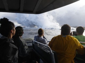 FILE - In this May 20, 2018 file photo, people watch a plume of steam as lava enters the ocean near Pahoa, Hawaii. Officials say an explosion sent lava flying through the roof of a tour boat off the Big Island, Monday, July 16, 2018, injuring at least 13 people. The people were aboard a tour boat that takes visitors to see lava from an erupting volcano plunge into the ocean.